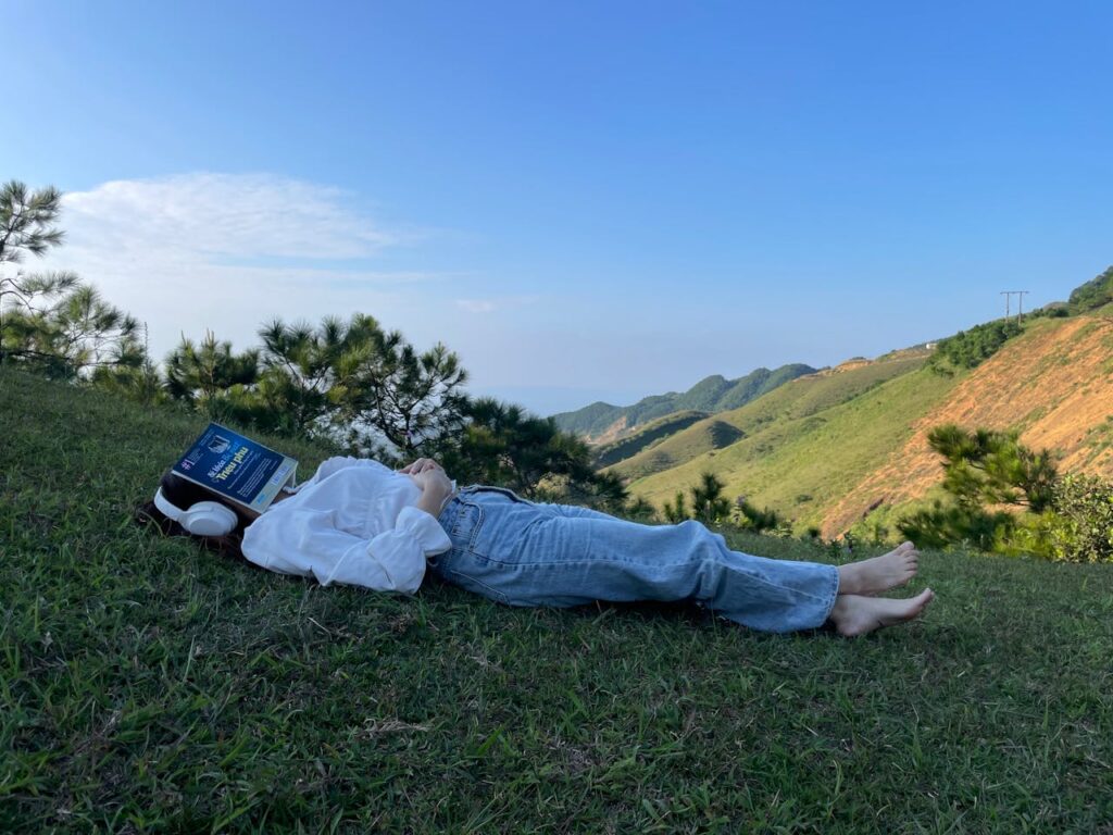 Woman in Headphones Lying Down with Book and Sleeping on Grass